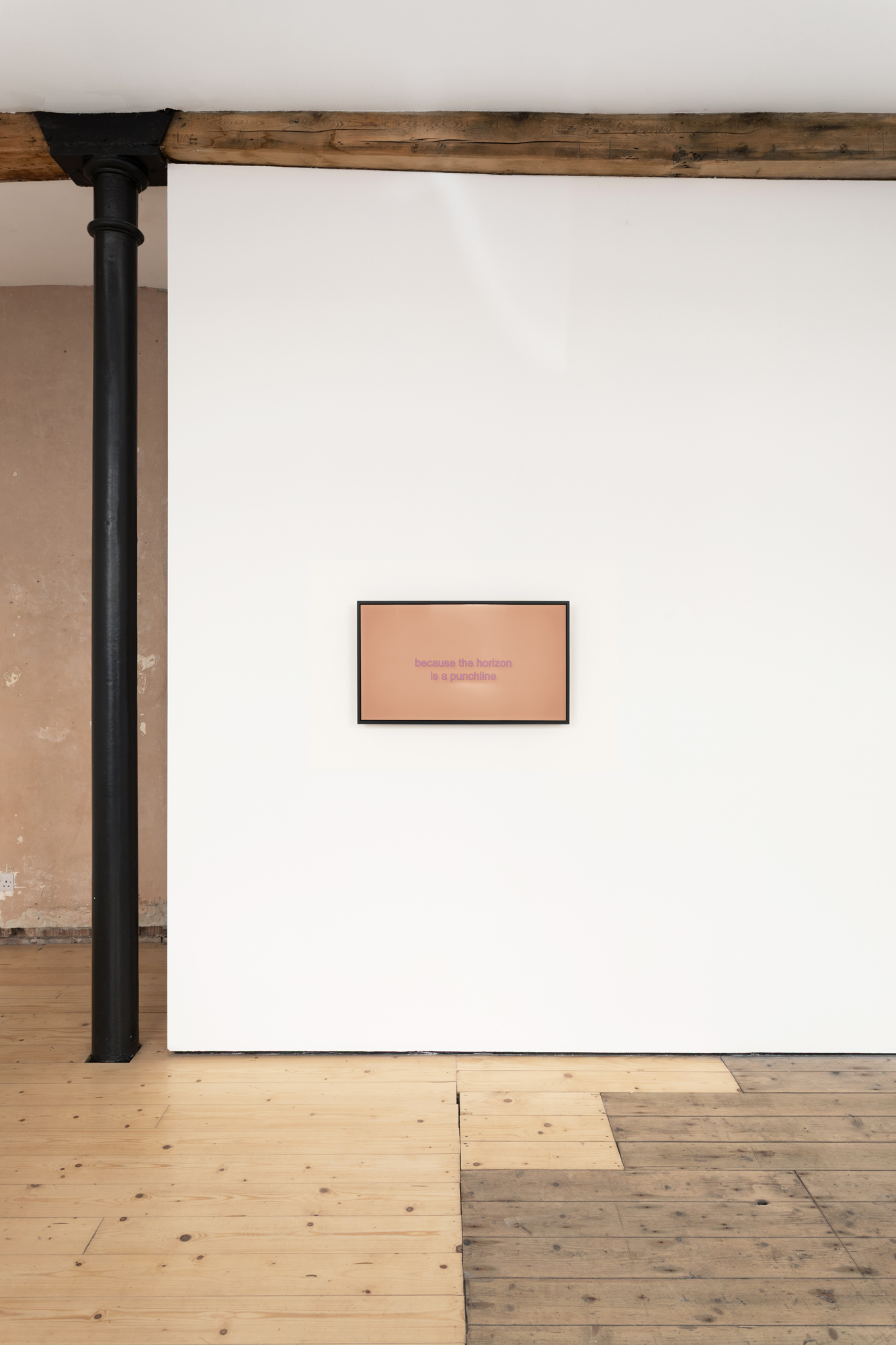 A screen placed on a white gallery wall, to the left of a dark grey pillar. The words 'because the horizon' appear on the screen.