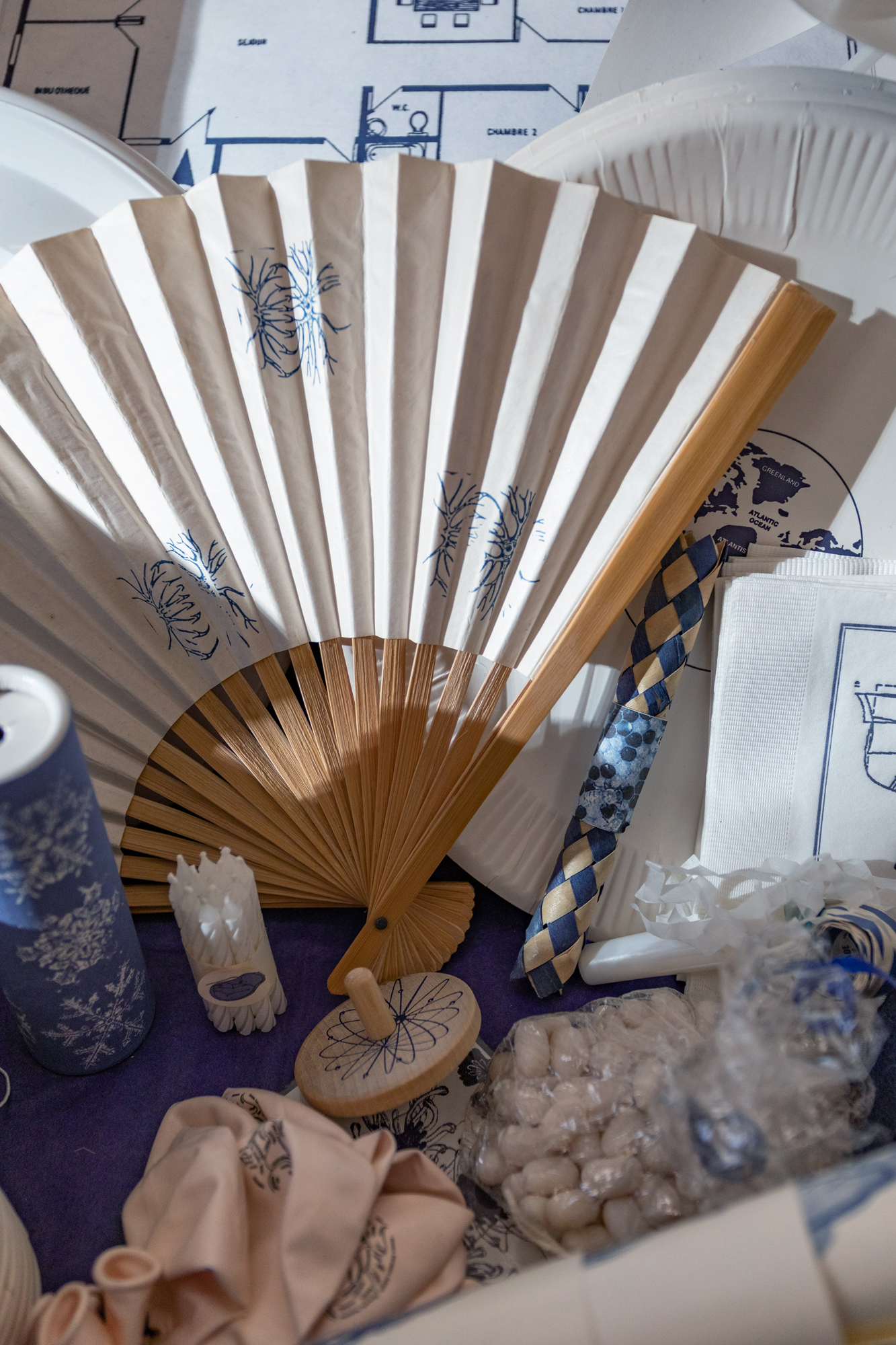 Party objects appearing against a dark blue tissue background, including a fan, container of confetti, un-inflated balloons, napkins, plates and a party trumpet.