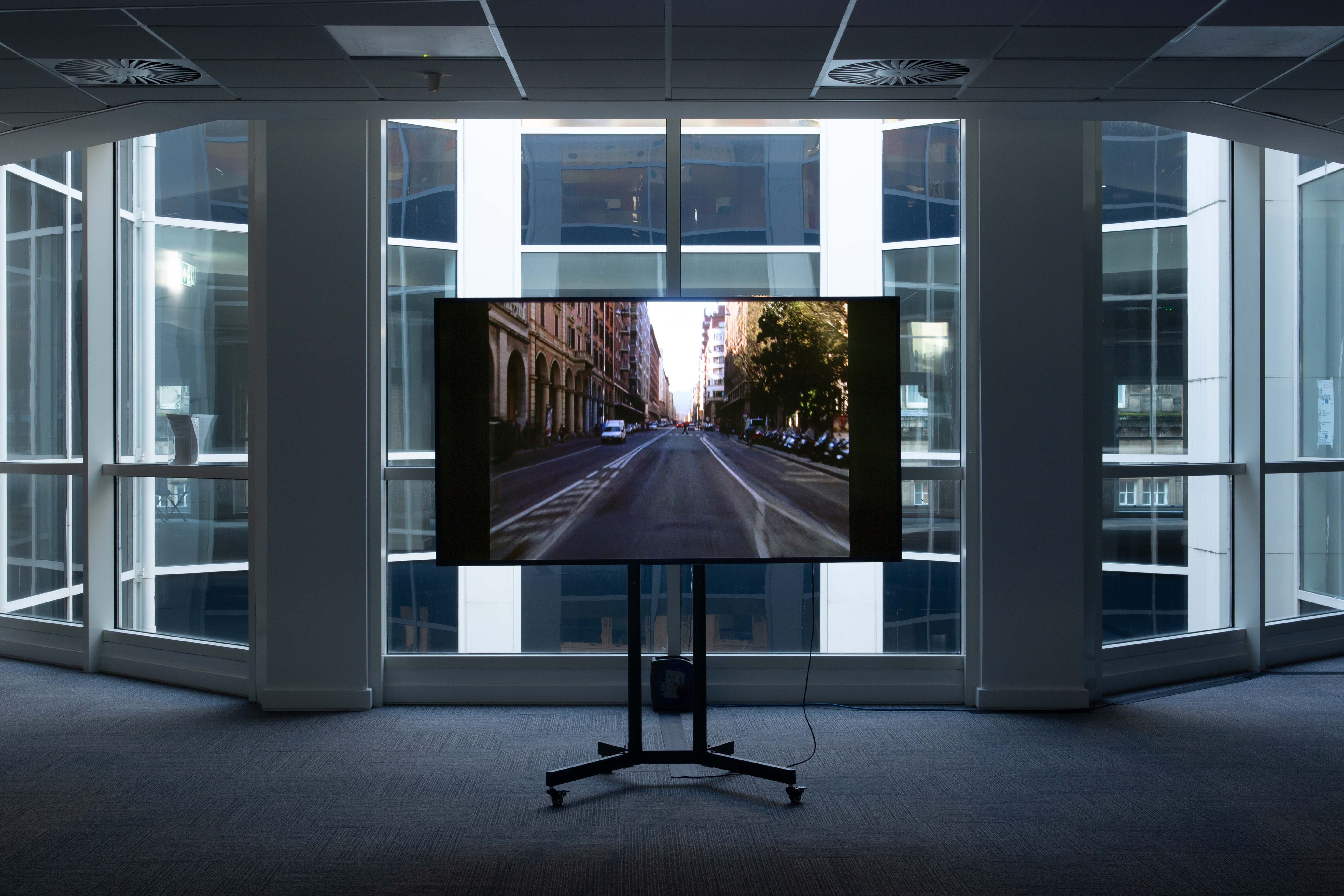 A television screen standing in an office space, against the backdrop of a large window.