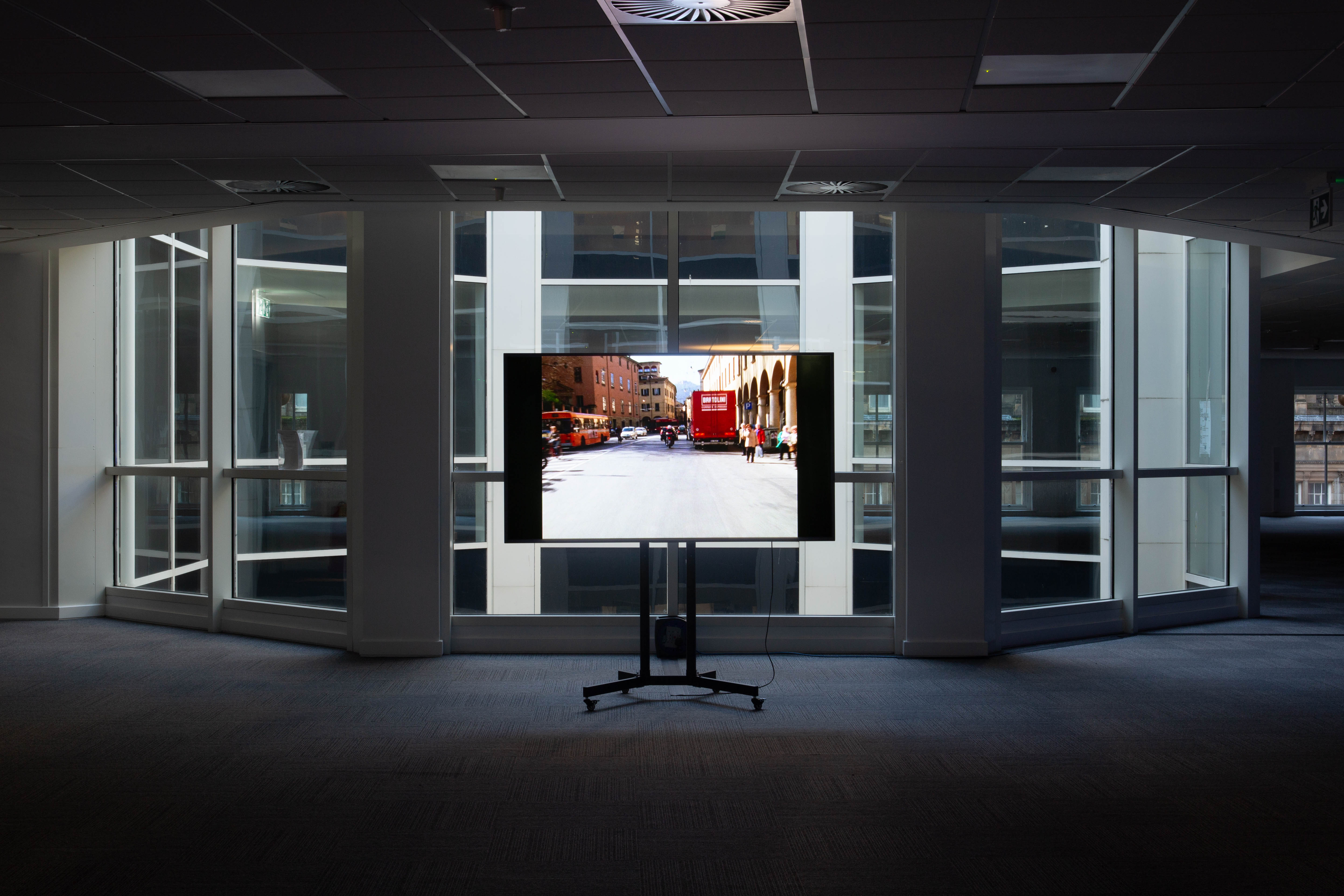A television screen standing in an office space, against the backdrop of a large window.