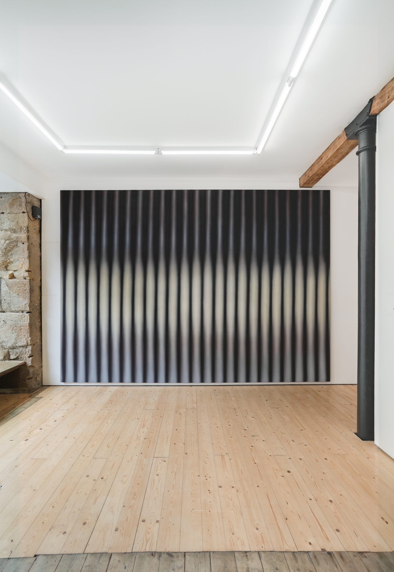 An abstract painting sits on a white gallery wall, with a wooden floor in the foreground.