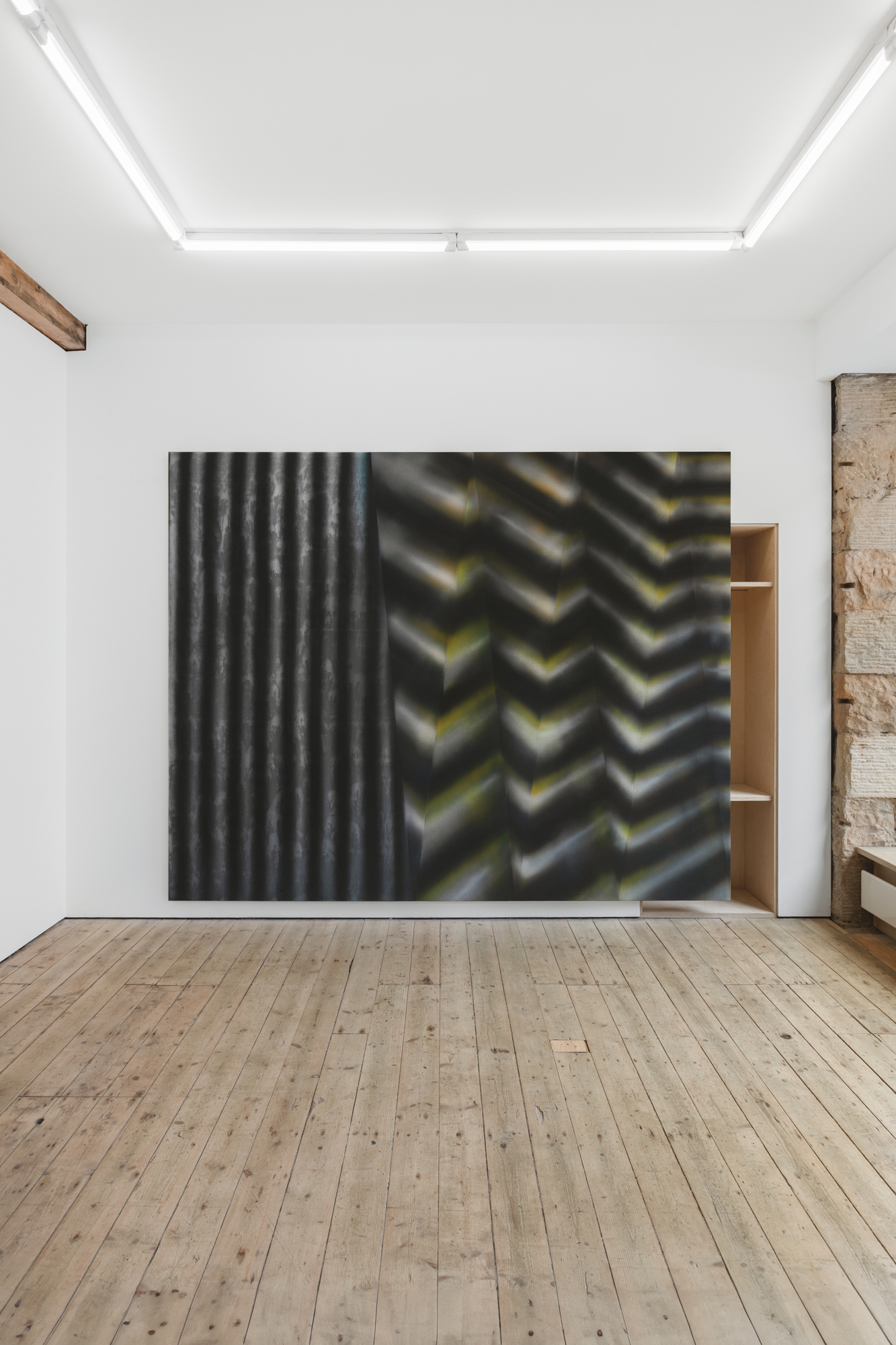 An abstract painting sits on a white gallery wall, with a wooden floor in the foreground.