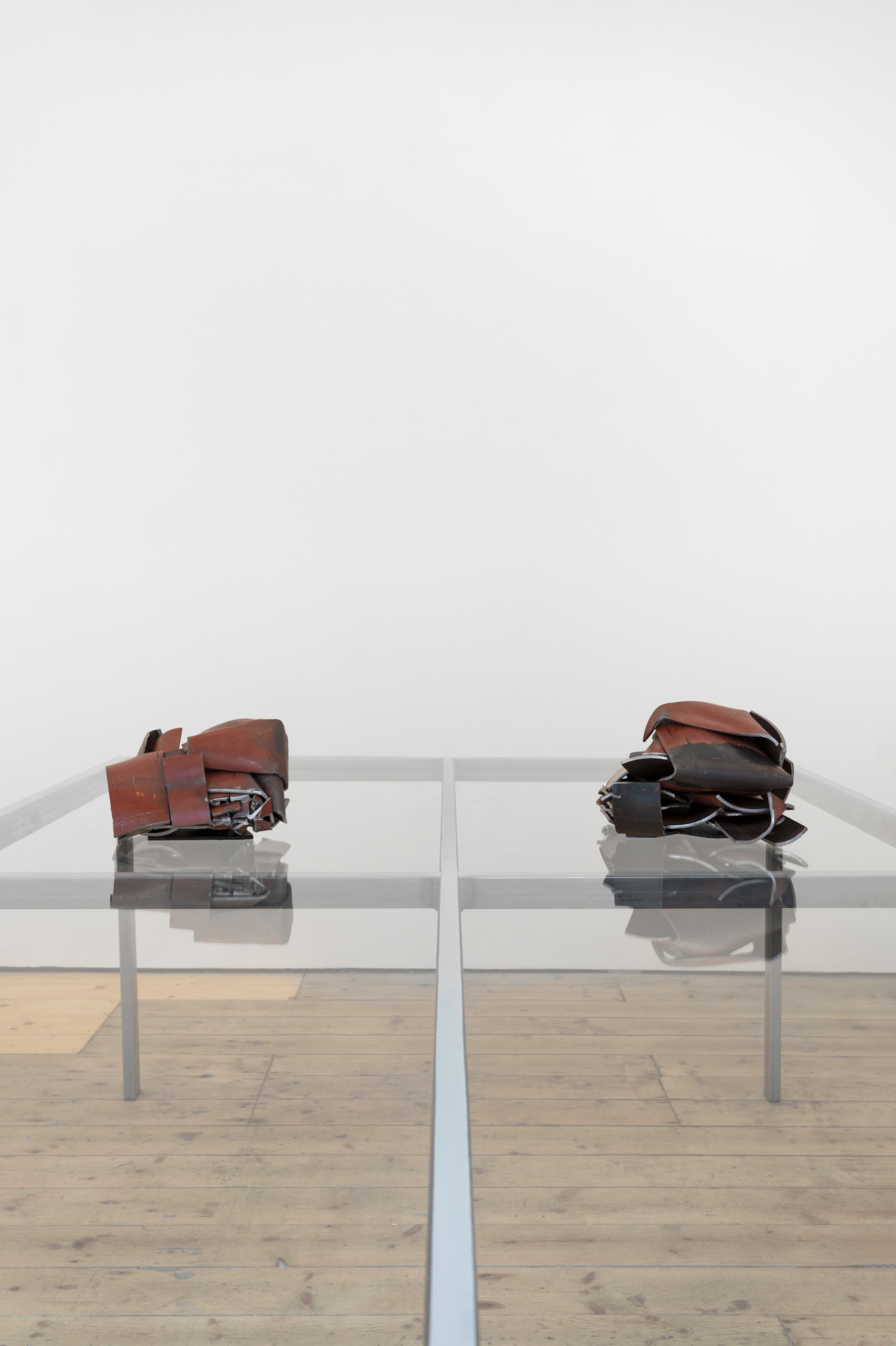 Two red metal sculptures sitting on a glass table, with reflections visible underneath.